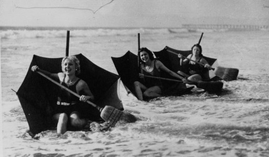 Acmé,  Sur une plage de Floride, jeunes filles se faisant porter par leur parapluie renversé formant un bateau et se servant d'un balai comme rame, 1932, photographie, Gallica/BnF